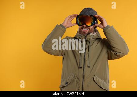 Wintersport. Glücklicher Mann in Skianzug und Schutzbrille auf orangem Hintergrund, Platz für Text Stockfoto