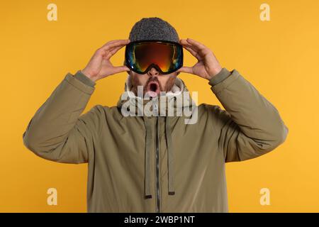 Wintersport. Emotionaler Mann in Skianzug und Brille auf orangem Hintergrund Stockfoto