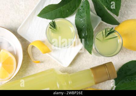 Leckerer Limoncello-Likör, Zitronen und grüne Blätter auf einem hellen, strukturierten Tisch, flach gelegen Stockfoto