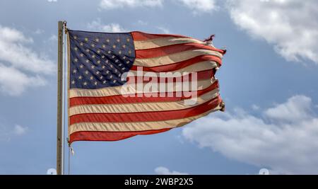 Die amerikanische Flagge reißt am Pol auf, blauer Himmel mit Wolken Stockfoto