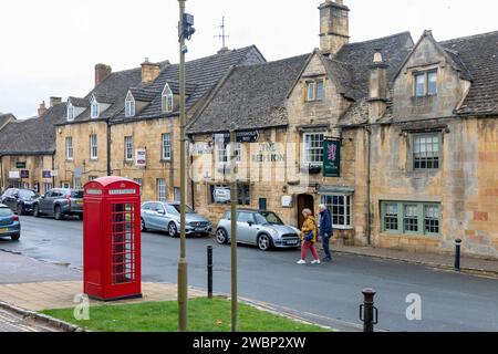 Der Red Lion Pub in der Chipping Campden High Street, traditionelle rote Londoner Telefonbox, Paar auf der anderen Straßenseite, England, UK, 2023 Stockfoto