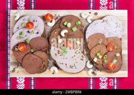 Dresden, Deutschland. Januar 2024. Brotscheiben mit verschiedenen veganen Würstchen liegen auf einem Holzbrett. Sie sind verzehrfertig, attraktiv verpackt und enthalten oft viel Zucker, Salz, Fett und Zusatzstoffe, aber nur wenige wichtige Nährstoffe. Stark verarbeitete Lebensmittel landen sehr oft im Warenkorb. Experten sehen Risiken im Zusammenhang mit hohem Konsum (dpa 'oft serviert, selten gesund: Hochprozessierte Lebensmittel') Credit: Sebastian Kahnert/dpa/Alamy Live News Stockfoto