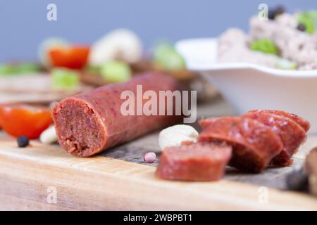 Dresden, Deutschland. Januar 2024. Brotscheiben mit verschiedenen veganen Würstchen, einer veganen Knoblauchwurst und einer Schüssel mit einer veganen Leberwurstalternative auf Erbsenbasis auf einem Holzbrett. Sie sind verzehrfertig, attraktiv verpackt und enthalten oft viel Zucker, Salz, Fett und Zusatzstoffe, aber nur wenige wichtige Nährstoffe. Stark verarbeitete Lebensmittel landen sehr oft im Warenkorb. Experten sehen Risiken im Zusammenhang mit hohem Konsum (dpa 'oft serviert, selten gesund: Hochprozessierte Lebensmittel') Credit: Sebastian Kahnert/dpa/Alamy Live News Stockfoto