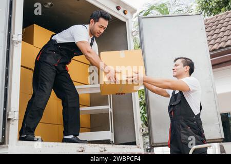 Teamwork in Aktion, Mitarbeiter des Umzugsdienstes entladen Kisten und Möbel vom Lkw in den neuen Stockfoto