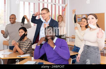 Glückliche Erwachsene Schüler, die Gesichtsschutzmasken im Klassenzimmer abnehmen Stockfoto