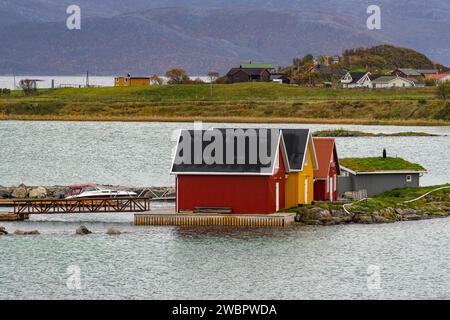 rote und gelbe Häuser am Strand des Atlantik auf der Insel Hillesøya bei Sommarøy, Troms, Norwegen. Landschaft Kalenderfoto mit Bergen im Hintergrund Stockfoto