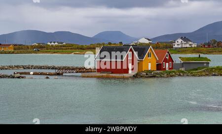 rote und gelbe Häuser am Strand des Atlantik auf der Insel Hillesøya bei Sommarøy, Troms, Norwegen. Landschaft Kalenderfoto mit Bergen im Hintergrund Stockfoto