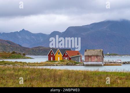 rote und gelbe Häuser am Strand des Atlantik auf der Insel Hillesøya bei Sommarøy, Troms, Norwegen. Landschaft Kalenderfoto mit Bergen im Hintergrund Stockfoto