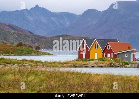 rote und gelbe Häuser am Strand des Atlantik auf der Insel Hillesøya bei Sommarøy, Troms, Norwegen. Landschaft Kalenderfoto mit Bergen im Hintergrund Stockfoto