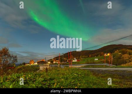 Wunderschöne grüne Nordlichter über einem Fjord und einem Haus auf der Insel Kvaloya in der Nähe von Tromsø. Tanzende Polarlichter über einem Berg, aurora borealis Stockfoto