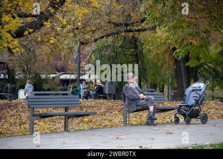 Großvater nimmt Enkel mit auf einen Spaziergang und ruht sich auf der Bank im öffentlichen Stadtpark aus Stockfoto