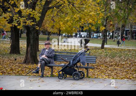 Großvater nimmt Enkel mit auf einen Spaziergang und ruht sich auf der Bank im öffentlichen Stadtpark aus Stockfoto