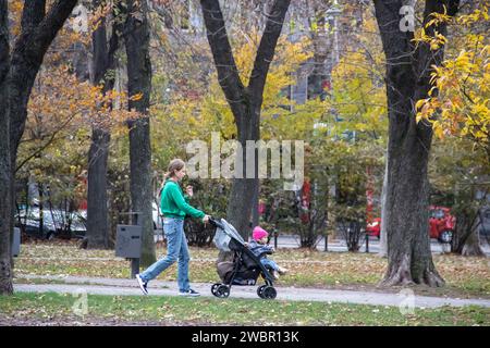 Junge Eltern (Mama), die ihr Kind im Herbst im Oktober in den öffentlichen Kinderpark mitnehmen Stockfoto