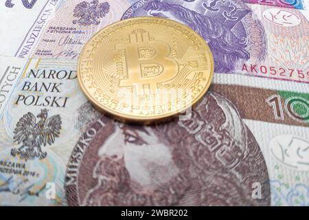 Nahaufnahme einer goldenen Bitcoin-Münze auf einem Stapel polnischer Złoty-Banknoten. Stockfoto