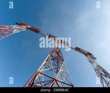 Sehr hohe elektrische Türme zur Übertragung von Hochspannungsstrom aus einem Kraftwerk vor blauem Himmel, aufgenommen mit einem Ultra-Weitwinkelobjektiv Stockfoto