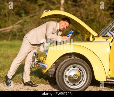 Lustige, ungewöhnliche, stilvolle, originelle Fotos mit Rollenumkehr eines jungen, attraktiven Brautpaares mit wunderschönen Veteranenautos in der Natur. Stockfoto