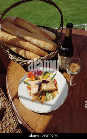 Frittiertes Filet von weißem Kabeljau mit saftigem Salat, Paprika, Zitrone, grünen Erbsen auf einem großen weißen Gericht auf einem Holztisch im Freien. Gesunde ausgewogene Ernährung Stockfoto