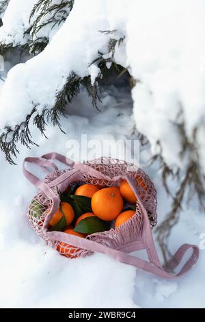 Netztasche mit Mandarinen im Schnee unter dem Weihnachtsbaum Stockfoto