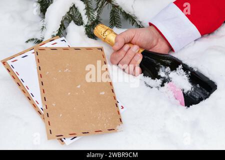 Weihnachtsbriefe und Weihnachtsmann Hand mit einer Flasche Champagner auf dem Schnee, Konzept zum Thema "schlechter Weihnachtsmann, der Kinderbriefe verliert" Stockfoto