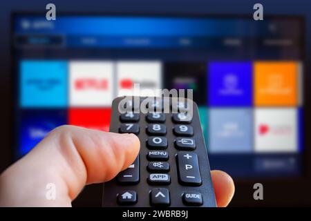 Ein Mann hält eine Fernbedienung eines Smart-TV in der Hand. Im Hintergrund sehen Sie den Fernsehbildschirm mit Streaming-Entertainment-Apps für Stockfoto