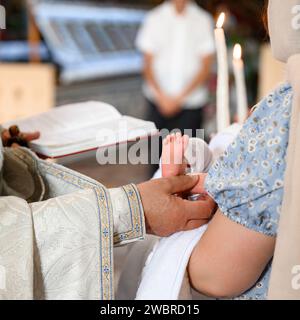 Der Priester vollbringt den Ritus der Taufe des Kindes und salbt das Bein mit heiligem Frieden. Stockfoto