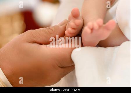 Der Priester vollbringt den Ritus der Taufe des Kindes und salbt das Bein mit heiligem Frieden. Stockfoto