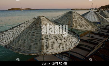 Ägäis und Mittelmeerküste bei Sonnenuntergang. Korbschirme und Sonnenliegen. Strandrestaurants. Palamutbuku Strände von Mugla, Turkiye. Stockfoto