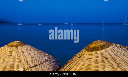 Ägäis und Mittelmeerküste bei Sonnenuntergang. Korbschirme und Sonnenliegen. Strandrestaurants. Palamutbuku Strände von Mugla, Turkiye. Stockfoto