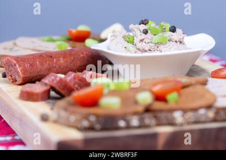 Dresden, Deutschland. Januar 2024. Brotscheiben mit verschiedenen veganen Würstchen, einer veganen Knoblauchwurst und einer Schüssel mit einer veganen Leberwurstalternative auf Erbsenbasis auf einem Holzbrett. Quelle: Sebastian Kahnert/dpa/Alamy Live News Stockfoto