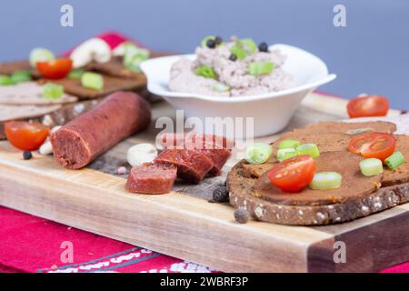 Dresden, Deutschland. Januar 2024. Brotscheiben mit verschiedenen veganen Würstchen, einer veganen Knoblauchwurst und einer Schüssel mit einer veganen Leberwurstalternative auf Erbsenbasis auf einem Holzbrett. Quelle: Sebastian Kahnert/dpa/Alamy Live News Stockfoto