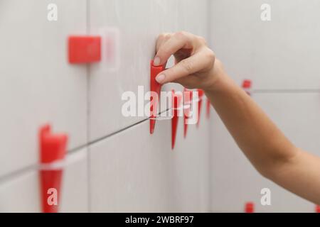 Frau, die die Wände des Badezimmers gefliest hat Flachwand-Nivelliersystem für Kunststofffliesen. Prozess der Installation von Fliesen im Badezimmer. Heimwerkerarbeit. Stockfoto