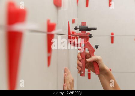 Frau, die die Wände des Badezimmers gefliest hat Flachwand-Nivelliersystem für Kunststofffliesen. Prozess der Installation von Fliesen im Badezimmer. Heimwerkerarbeit. Stockfoto