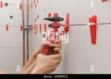 Frau, die die Wände des Badezimmers gefliest hat Flachwand-Nivelliersystem für Kunststofffliesen. Prozess der Installation von Fliesen im Badezimmer. Heimwerkerarbeit. Stockfoto