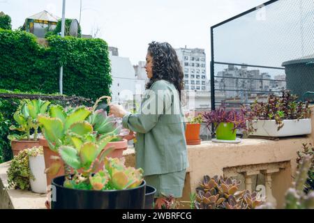 Lateinische Frau mit Lockenwicklern, die mittags im Garten steht und sich um Blumen und Pflanzen kümmert, Kopierraum Stockfoto