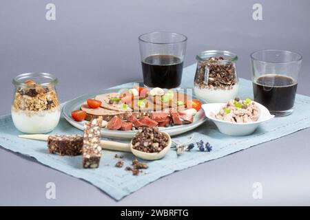 Dresden, Deutschland. Januar 2024. Eine Brotscheibe mit verschiedenen veganen Würstchen, eine vegane Knoblauchwurst und eine Schüssel mit einer veganen Leberwurstalternative auf Erbsenbasis, Müsli mit pflanzlicher Joghurtalternative, Cashew Dattelbar und Kaffee auf einem Tisch. Quelle: Sebastian Kahnert/dpa/Alamy Live News Stockfoto