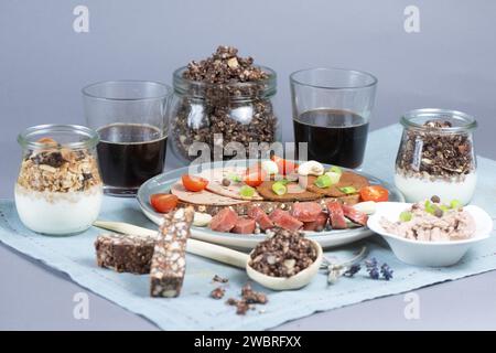 Dresden, Deutschland. Januar 2024. Eine Brotscheibe mit verschiedenen veganen Würstchen, eine vegane Knoblauchwurst und eine Schüssel mit einer veganen Leberwurstalternative auf Erbsenbasis, Müsli mit pflanzlicher Joghurtalternative, Cashew Dattelbar und Kaffee auf einem Tisch. Quelle: Sebastian Kahnert/dpa/Alamy Live News Stockfoto