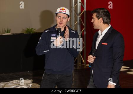 Birmingham, Großbritannien. Januar 2024. Die Lackierung des M Sport Ltd World Rally Championship Car. Fahrer Adrien Fourmaux (links) plaudert mit Moderator Bryn Lucas, nachdem er die Vorhänge des Red Bull liverisierten Ford Performance-Motors auf der Autosport International Show hochgezogen hatte. Credit Milo Chandler/Alamy Live Stockfoto