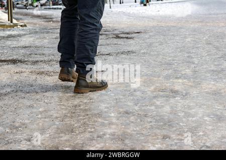 Der Mann läuft auf gefährlich eisigen Gehwegen mit wenig Sand Stockfoto