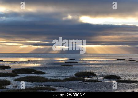 Die Sonnenstrahlen einer Morgensonne, die durch die Wolken scheint, auf eine Ebbe an der Küste von Barrow in Furness. Stockfoto