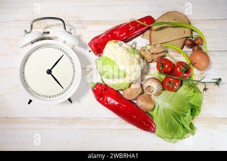 Intervallfasten oder IF, Lebensmittel und ein Wecker geben die Zeit an, während der es essen darf, Diät Konzept für Gewichtsverlust Stockfoto