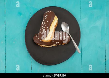 Zwei Eclair-Kuchen auf einer schwarzen Keramikplatte und blauer Holzbretttisch Stockfoto