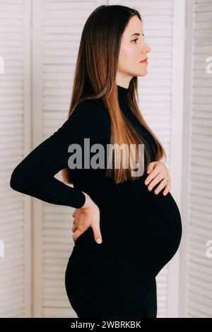 Elegante Erwartung: Ein Profil von Stärke und Gnade. Schwangere Frau im schwarzen engen Kleid. Wunderschöne Silhouette Stockfoto