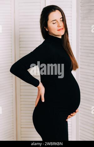 Elegante Erwartung: Ein Profil von Stärke und Gnade. Schwangere Frau im schwarzen engen Kleid. Wunderschöne Silhouette Stockfoto