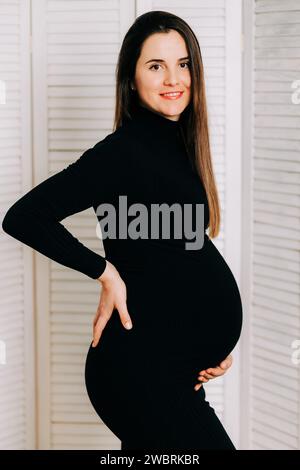 Elegante Erwartung: Ein Profil von Stärke und Gnade. Schwangere Frau im schwarzen engen Kleid. Wunderschöne Silhouette Stockfoto