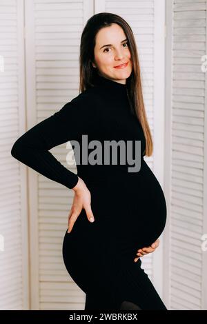 Elegante Erwartung: Ein Profil von Stärke und Gnade. Schwangere Frau im schwarzen engen Kleid. Wunderschöne Silhouette Stockfoto