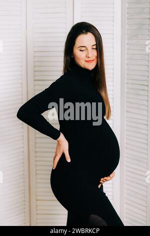 Elegante Erwartung: Ein Profil von Stärke und Gnade. Schwangere Frau im schwarzen engen Kleid. Wunderschöne Silhouette Stockfoto