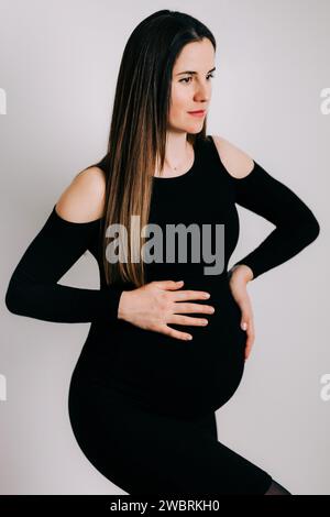 Elegante Erwartung: Ein Profil von Stärke und Gnade. Schwangere Frau im schwarzen engen Kleid. Wunderschöne Silhouette Stockfoto