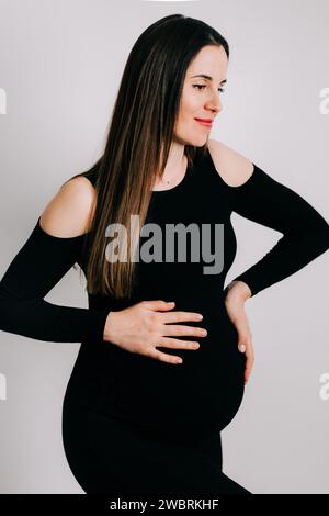 Elegante Erwartung: Ein Profil von Stärke und Gnade. Schwangere Frau im schwarzen engen Kleid. Wunderschöne Silhouette Stockfoto