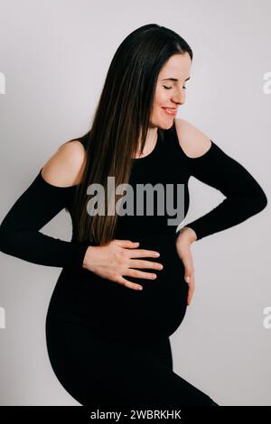 Elegante Erwartung: Ein Profil von Stärke und Gnade. Schwangere Frau im schwarzen engen Kleid. Wunderschöne Silhouette Stockfoto