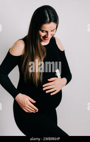 Elegante Erwartung: Ein Profil von Stärke und Gnade. Schwangere Frau im schwarzen engen Kleid. Wunderschöne Silhouette Stockfoto